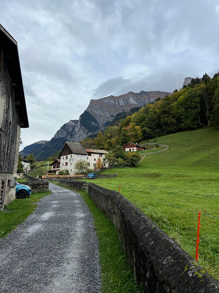 On the Heidiweg Heidi trail hiking trail Heididorf Switzerland, a gravel path with a stone wall alongside it, houses in the distance and mountain vistas 