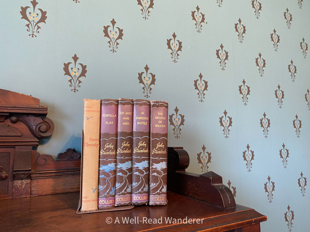 steinbeck novels on display in front of blue wallpaper at steinbeck house