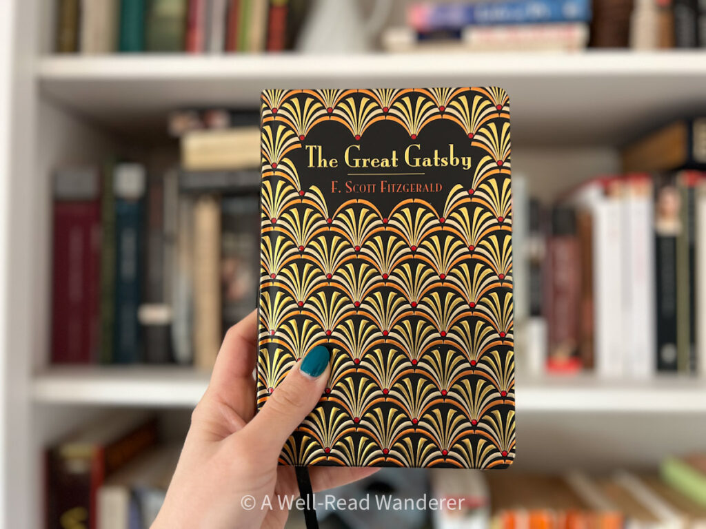 the great gatsby by f scott fitzgerald, foiled cover, held by a hand in front of a bookshelf