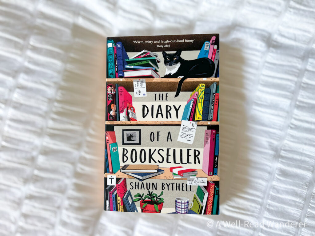 the diary of a bookseller by shaun bythell colorful bookshelf on cover, book on white duvet