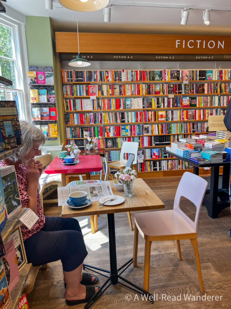 interior of waterstones bookstore and cafe in lewes uk, bookshelves, cafe tables, woman sits eating and reading