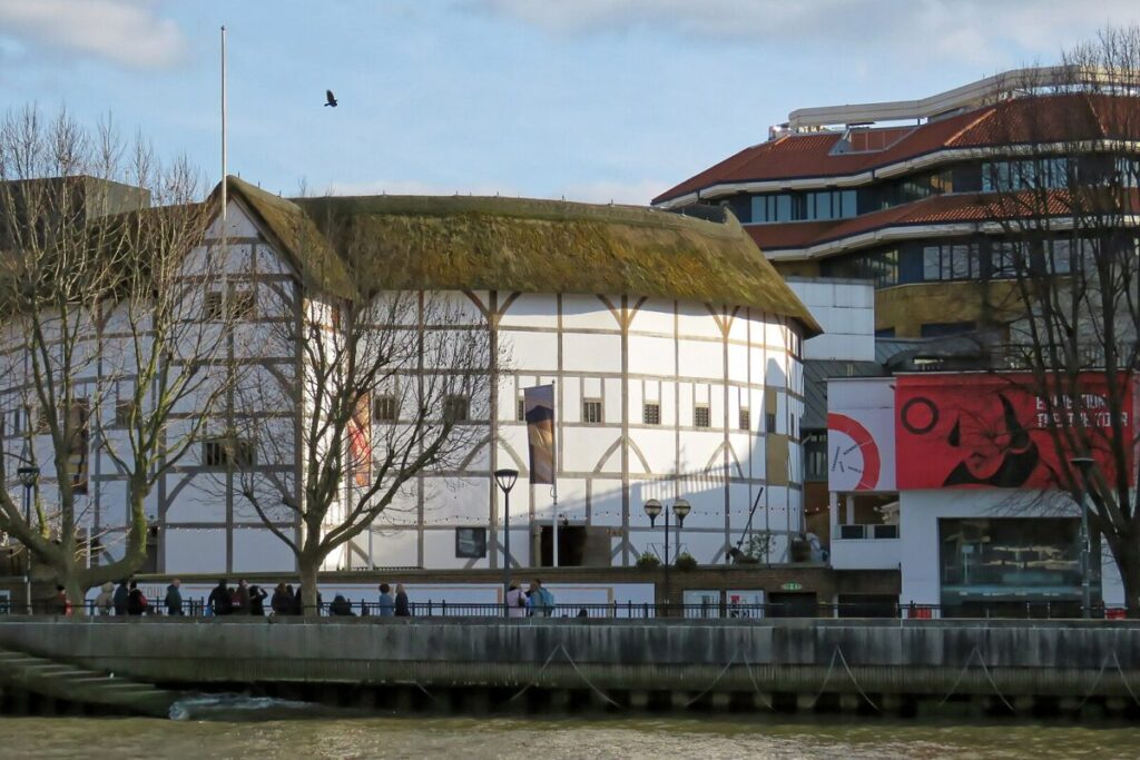 exterior of the globe theatre in london. white half timbered octagonal building along the river and with bare winter trees in foreground. Photo by Acabashi, Creative Commons license
