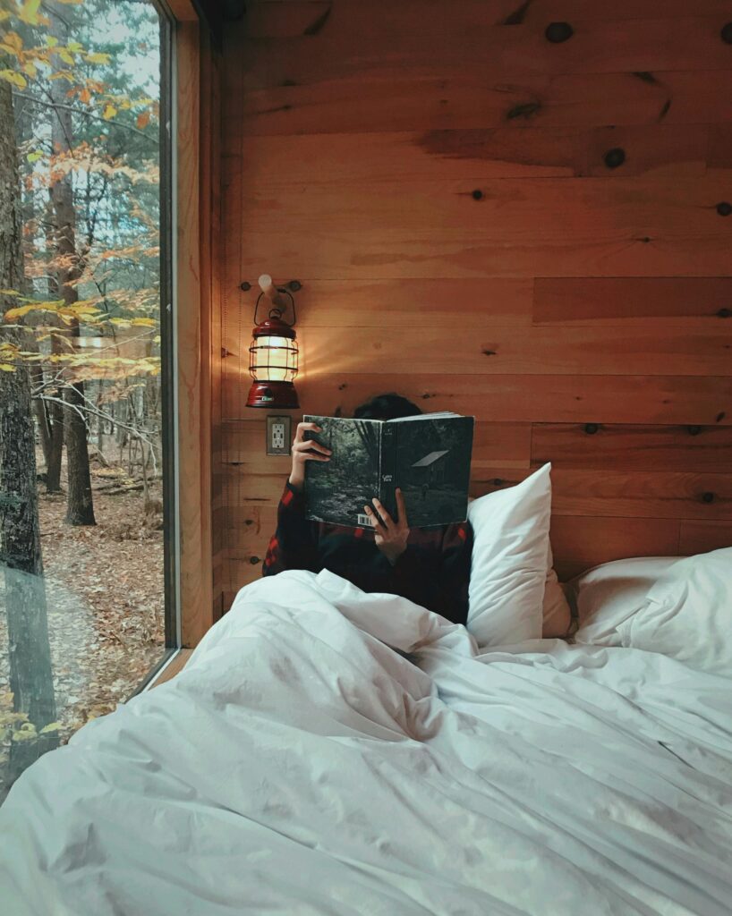 Person comfortably reading in a warm wooden cabin with a scenic fall view.
