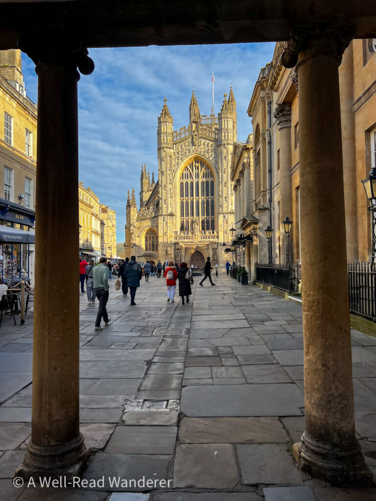 view of bath abbey through foreground pillars, cathedral has gothic facade, tan flagstone pathway to front