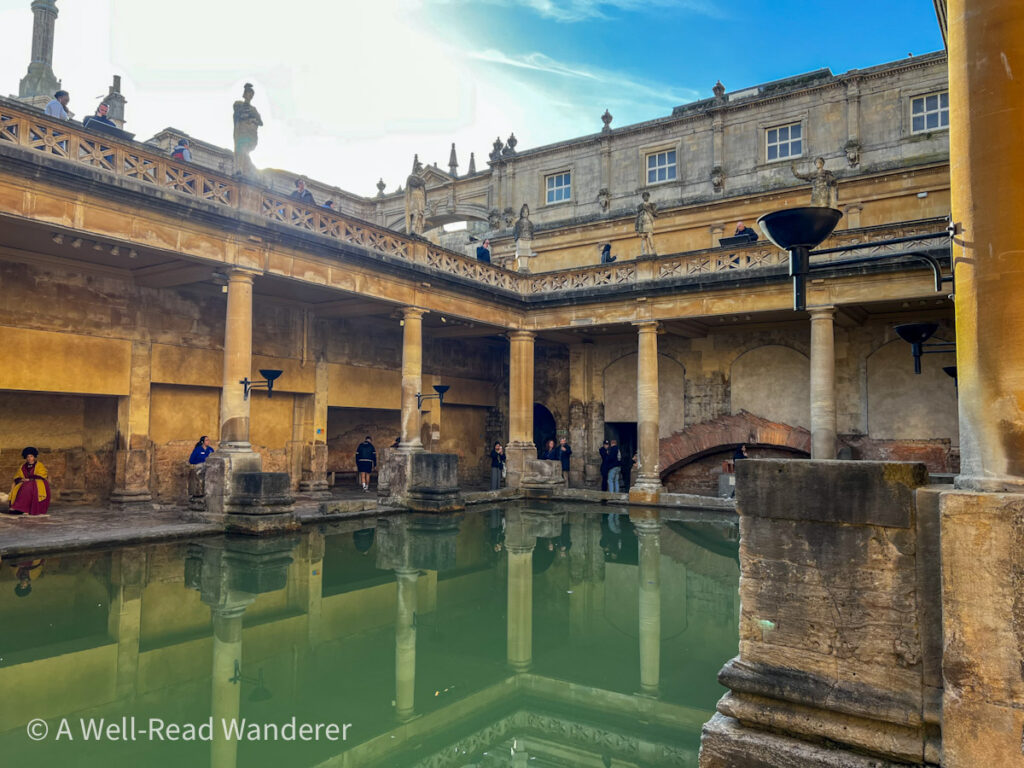 roman baths in bath uk with green mineral water in foreground surrounded by ancient roman pillars and terrace