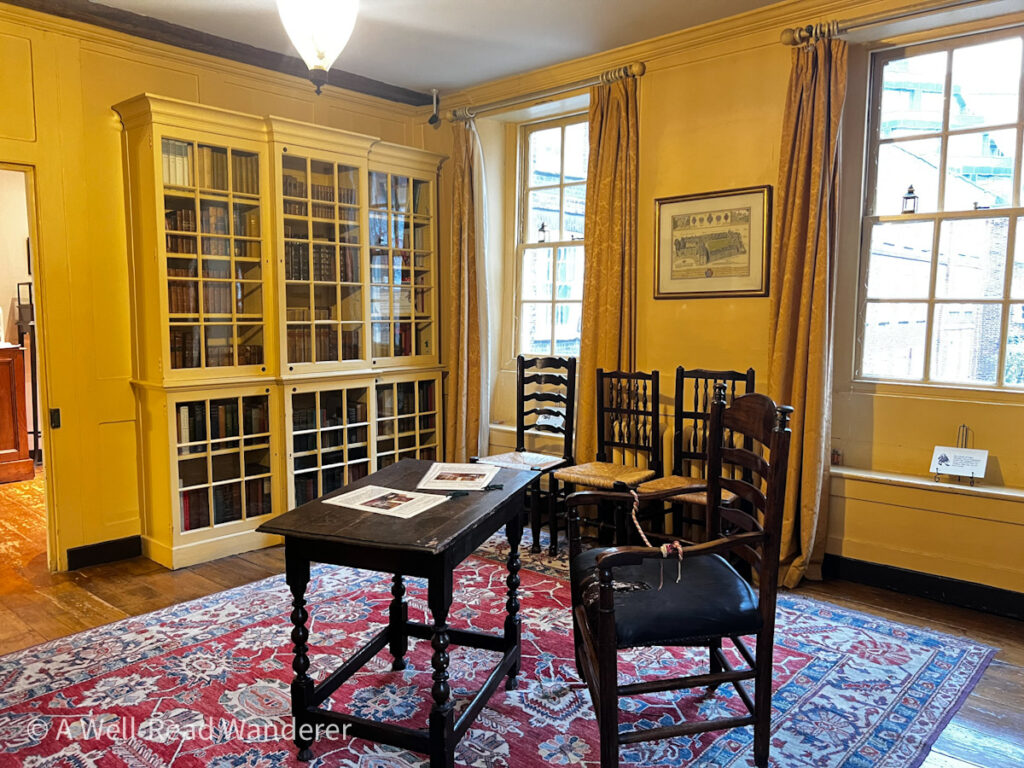 yellow library inside dr johnsons house london with a wooden simple table desk in the center of the room and walls lined with glass fronted bookshelves
